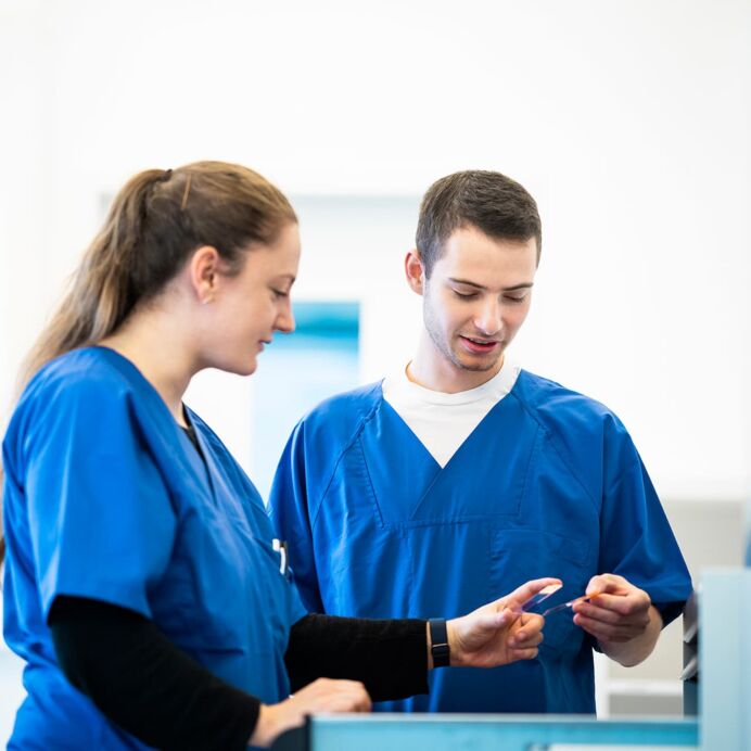 Zwei Laboranten in blauer Arbeitskleidung diskutieren über eine Probe in einem hellen Laborraum.