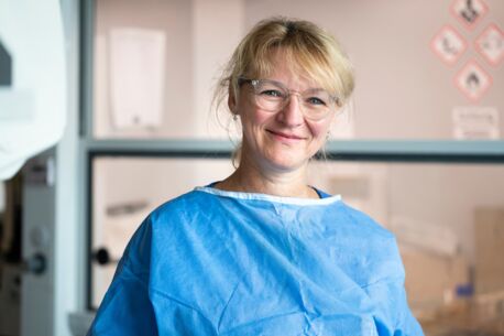 Portrait einer lächelnden Frau in blauer Schutzkleidung und Brille in einem Labor.